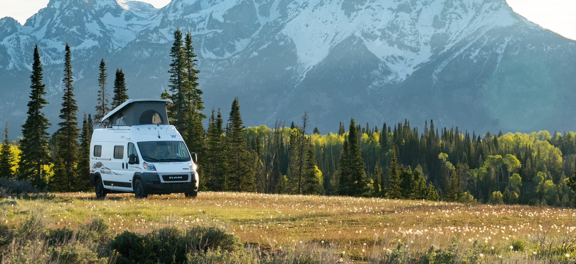 Winnebago Solis campervan parked in a mountain meadow with the Rocky Mountains in the background